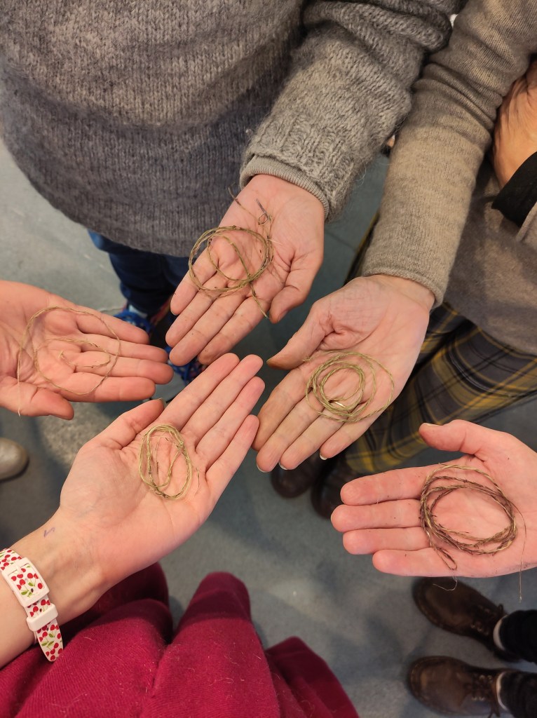Several hands holding nettle thread in their palms
